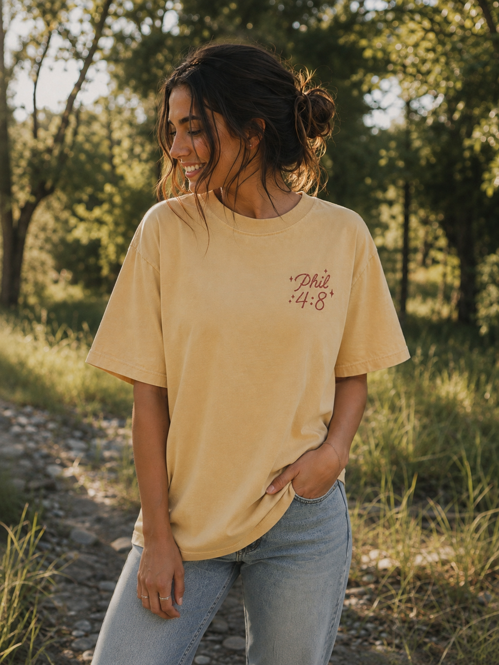 Woman wearing the Cotton Collective Vintage Sunflower oversized tee with "Philippians 4:8" on the left chest, styled with light wash jeans outdoors.