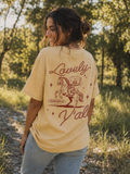 Cotton Collective Vintage Sunflower oversized tee, back view, worn outdoors: a cowboy on a rearing horse with a lasso graphic, "Lovely" scripted above, a "Philippians 4:8" badge, and "Y'all" scripted below.